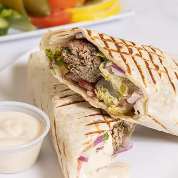 Two grilled wraps filled with meat, lettuce, and red onion, with a side of sauce and salad.