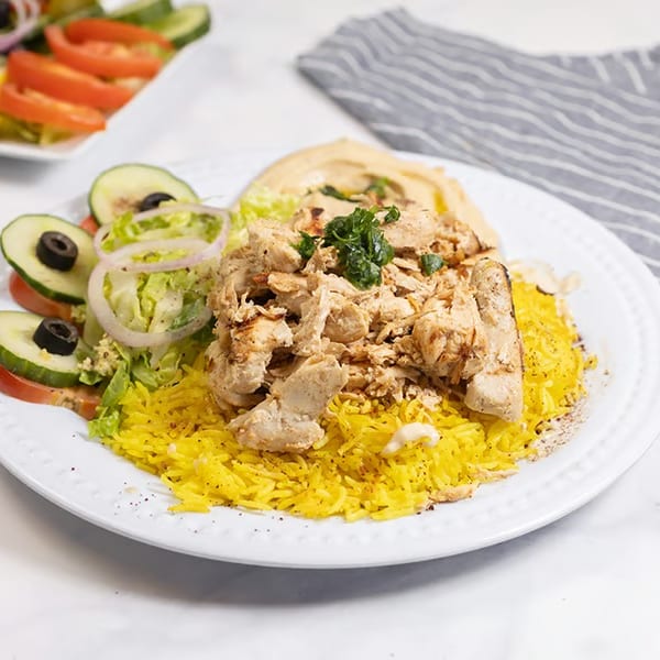 Chicken shawarma plate with yellow rice, hummus, and a side salad with cucumbers, tomatoes, and olives.