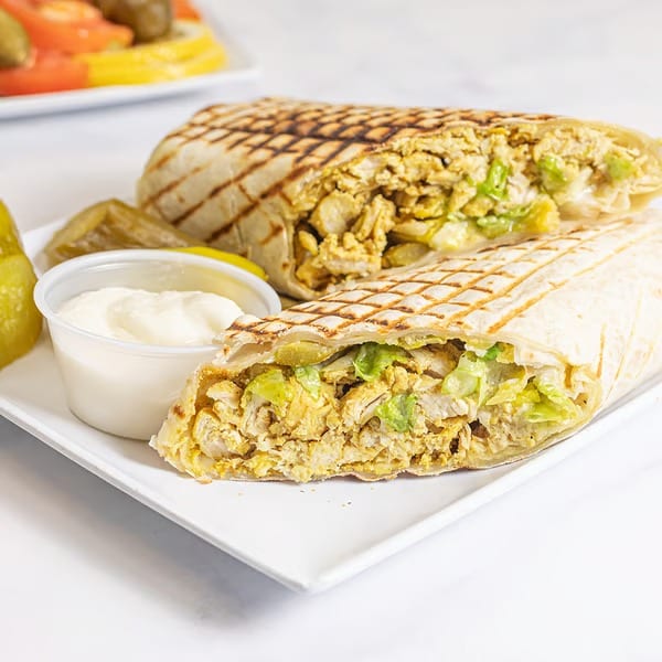 Two grilled chicken shawarma wraps, one cut in half, with a side of pickles and white sauce.