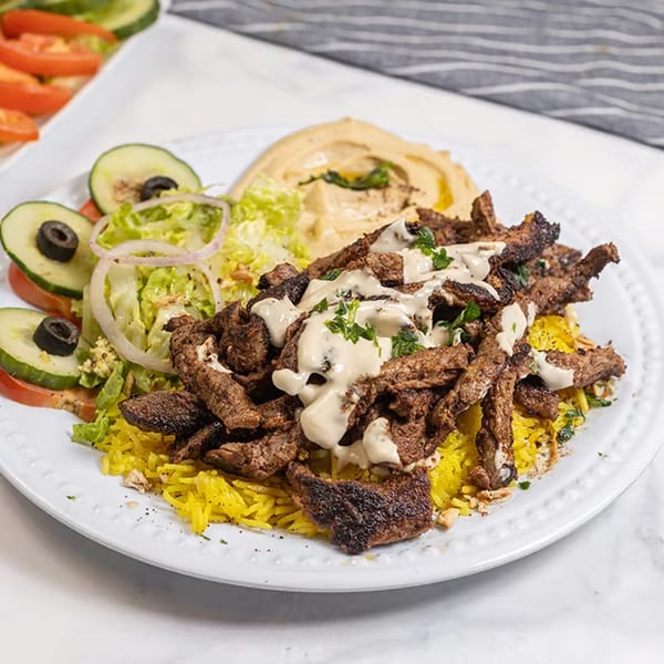 Shawarma plate with yellow rice, meat, hummus, and a side salad with cucumbers and tomatoes.
