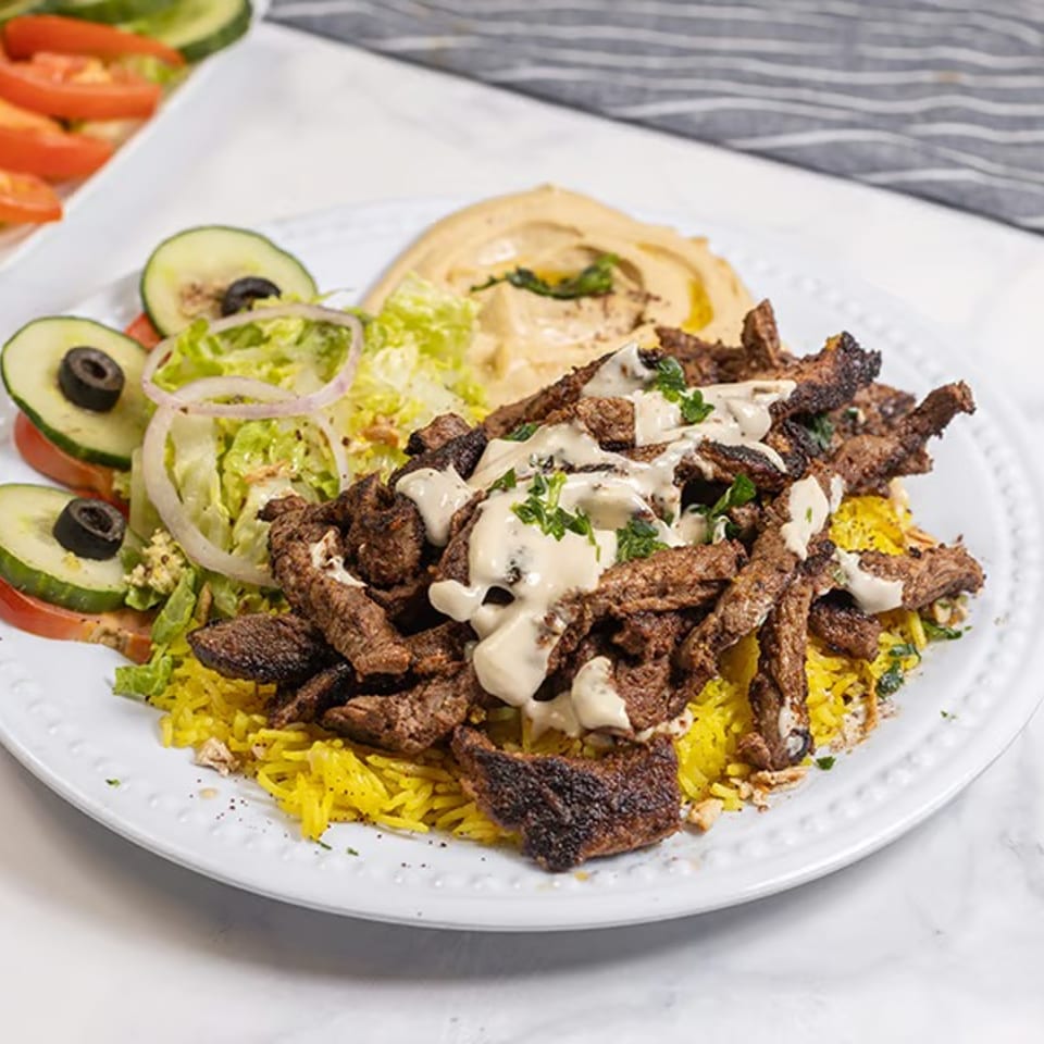 Shawarma plate with yellow rice, meat, hummus, and a side salad with cucumbers and tomatoes.