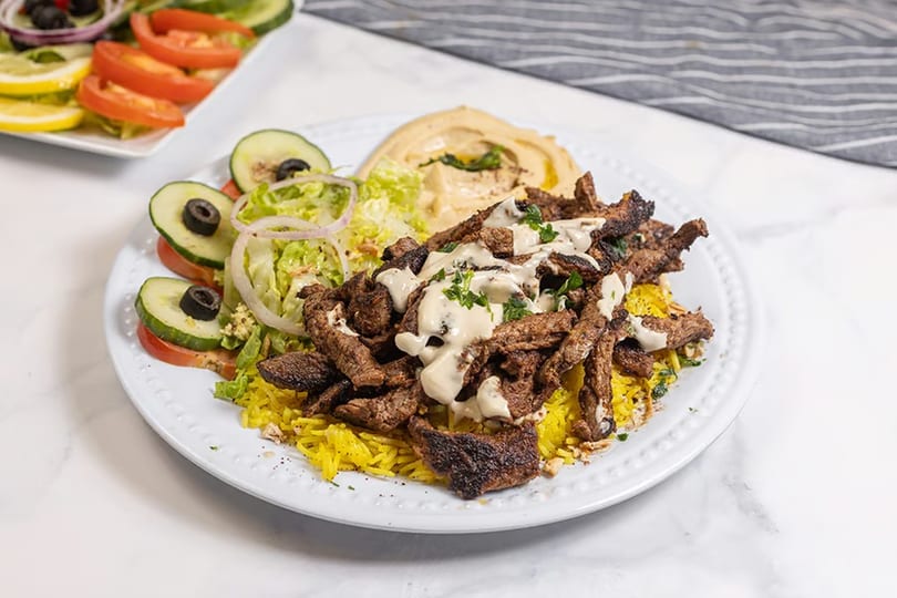 Shawarma plate with yellow rice, meat, hummus, and a side salad with cucumbers and tomatoes.