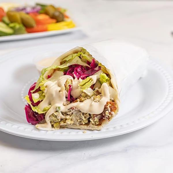 A falafel wrap with lettuce, red cabbage, and tahini sauce on a white plate with a side salad.