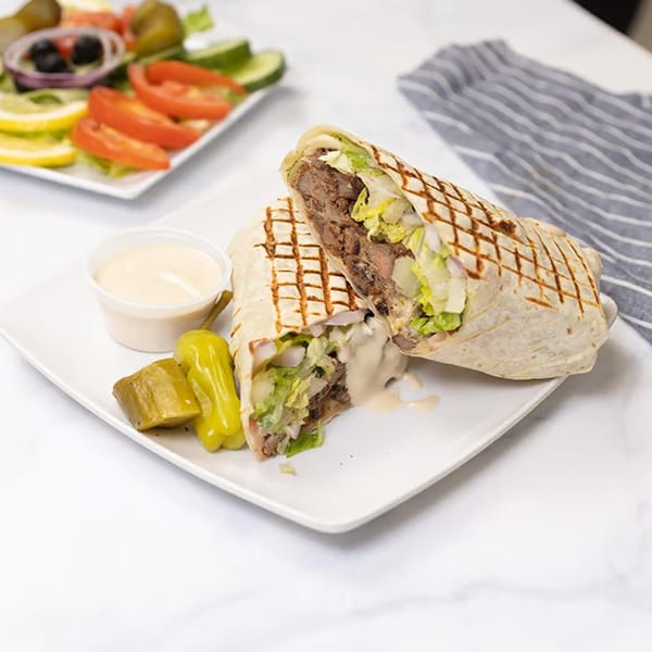 Grilled wrap with meat, lettuce, and sauce, served with pickles and a side salad.