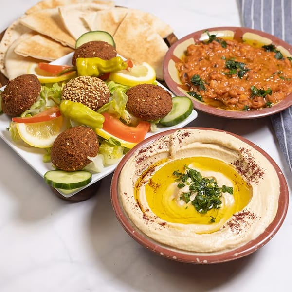 A platter of falafel, salad, pita bread, hummus, and a bowl of ful medames.