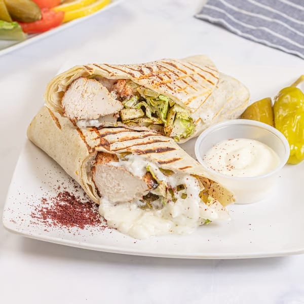 Two chicken shawarma wraps with sauce, pickles, and a side salad on a white plate.
