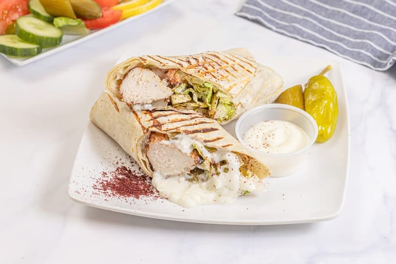 Two chicken shawarma wraps with sauce, pickles, and a side salad on a white plate.